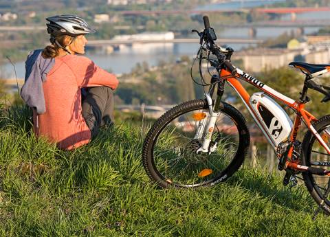 Eine Junge Frau, die neben ihrem Fahrrad auf einem Berg sitzend auf die Stadt blickt.